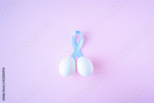 prostate cancer, healthcare, profession, medicine concept - close up of chicken white eggs and blue ribbon in penis shape on bright background. Cancer awareness, cure, men carcinoma