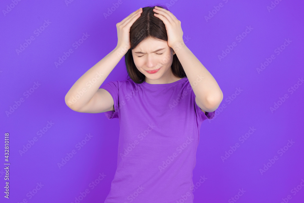 young beautiful Caucasian woman wearing purple T-shirt over purple wall holding head with hands, suffering from severe headache, pressing fingers to temples young beautiful Caucasian woman wearing purple T-shirt over purple wall holding head with hands, suffering from severe headache, pressing fingers to temples