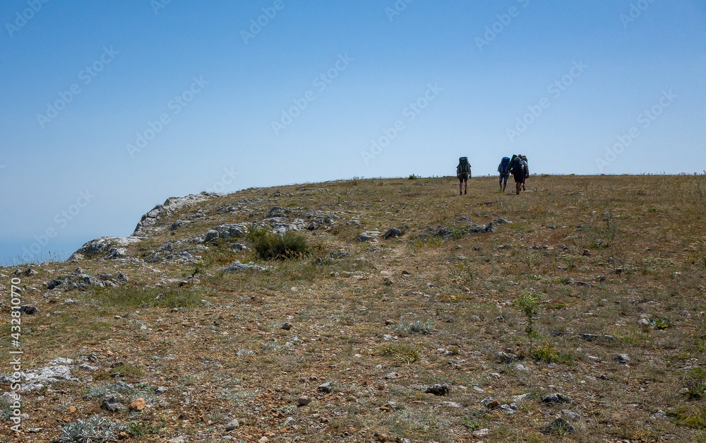 A group of tourists with backpacks on the top of the steppe plateau on a hot summer day.