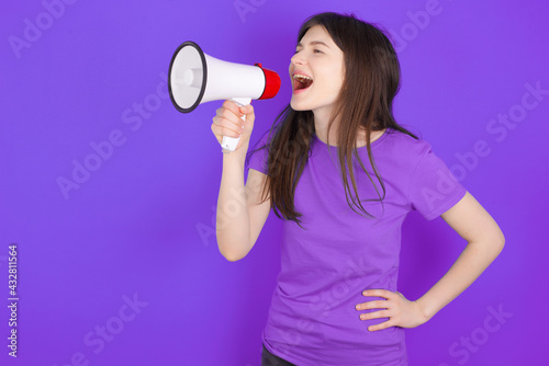 Funny young beautiful Caucasian girl wearing purple T-shirt over purple background People sincere emotions lifestyle concept. Mock up copy space. Screaming in megaphone.