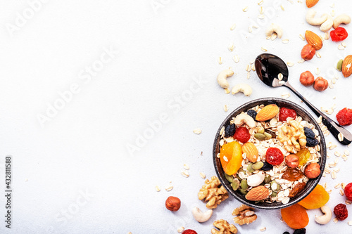 Muesli bowl and organic ingredients for healthy breakfast. Granola, nuts, dried fruits, oatmeal, whole grain flakes on white table