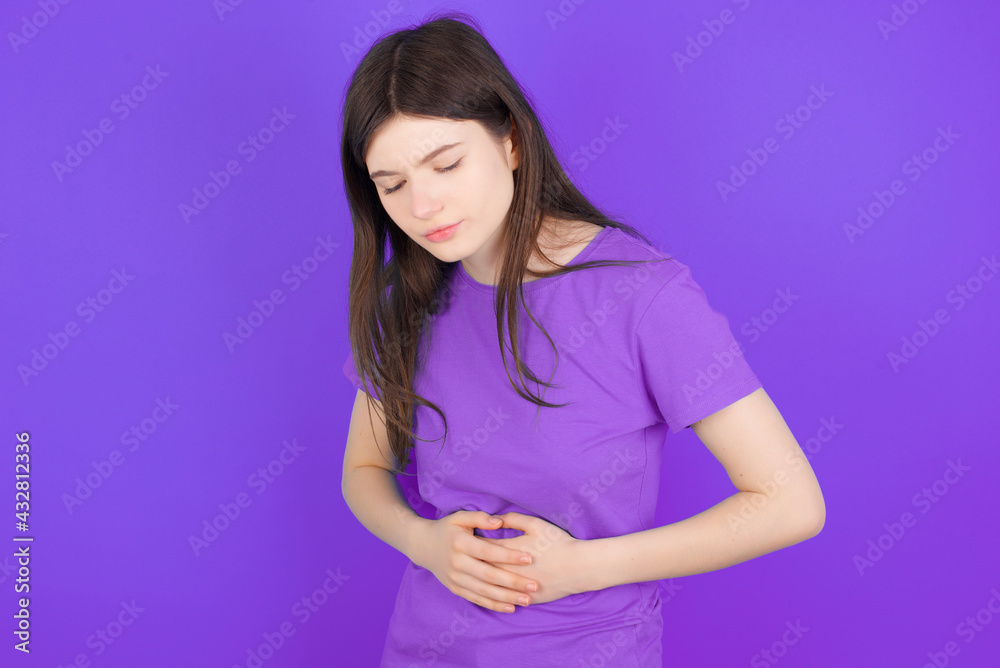 young beautiful Caucasian girl wearing purple T-shirt over purple background got stomachache young beautiful Caucasian girl wearing purple T-shirt over purple background got stomachache