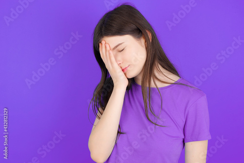 young beautiful Caucasian girl wearing purple T-shirt over purple background with sad expression covering face with hands while crying. Depression concept.