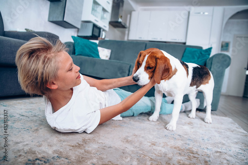 Cute little boy playing with dog on floor at home - Child kissing it's pet friend lying on carpet - Kids and dogs concept 