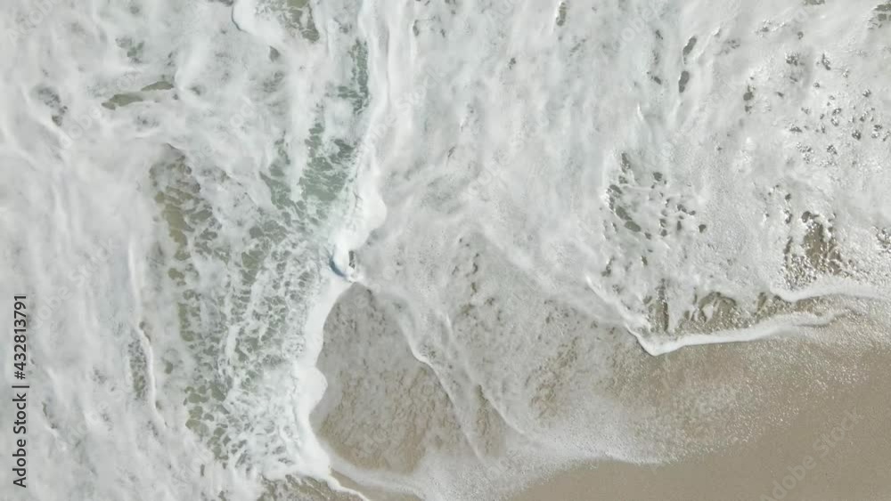Still drone shot above beach sand as ocean water wash over it