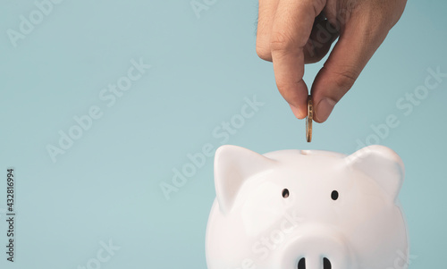 Fotografia Hand putting coin to white piggy bank saving on blue background and copy space , Money saving for future investment and retirement concept