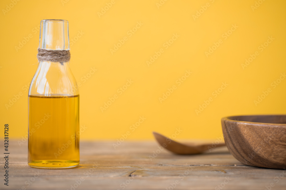 Olive oil in a bottle, a spoon, a plate on a wooden table on a yellow background. Copy space. Olive oil in a bottle, a spoon, a plate on a wooden table on a yellow background. Copy space.