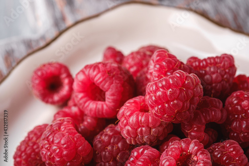 Raspberry fruits in white plate, healthy pile of summer berries, angle view macro