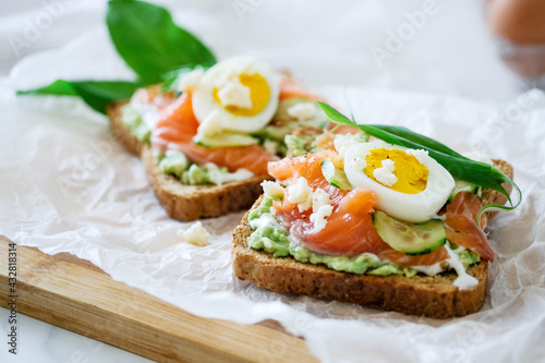 Open sandwich traditional danish smorrebrod salmon, cucumber, boiled egg, soft cheese. Homemade sandwich with rye bread on white background, top view. Tasty salmon fish sandwich closeup photo