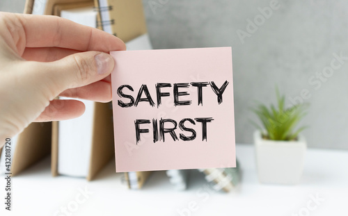 Safety first in unsafe workplace concept photo. Hand of staff is holding the text sign with blurred background of drilling rig or refinery plant equipment at worksite location.