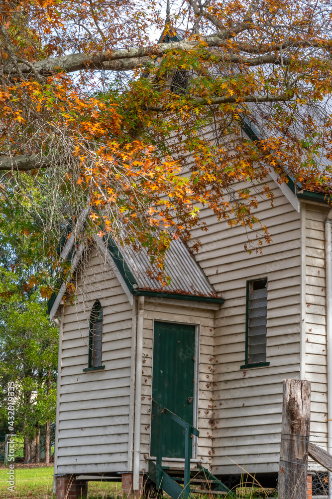 Small quaint disused rural white weatherboard church front entrance surrounded by autumnal trees