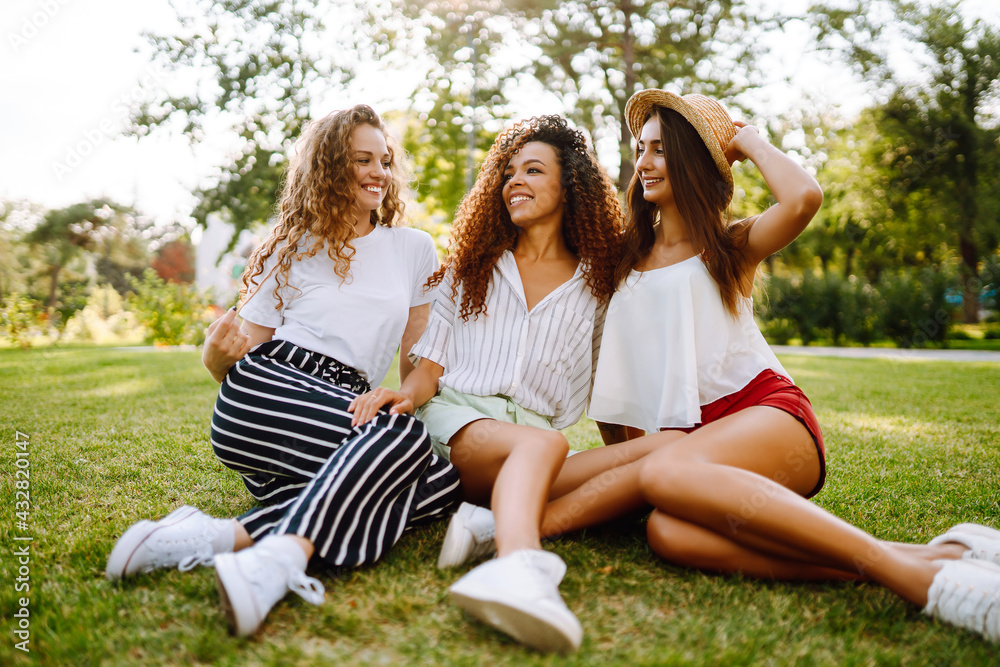 Three young woman relaxing on the grass. Young friends laughing and enjoying holidays together. Friendship, youth and travel concept. Three young woman relaxing on the grass. Young friends laughing and enjoying holidays together. Friendship, youth and travel concept.