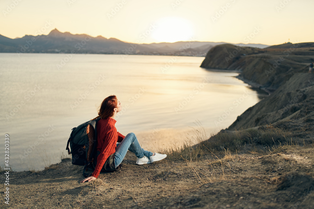 the traveler sits on the sand in the mountains and relaxes near the sea at sunset