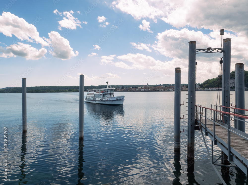 ferry that connects the shores of the lake arrives at the pier. summer panorama of Lake Maggiore with large white clouds reflected on the water. ferry that connects the shores of the lake arrives at the pier. summer panorama of Lake Maggiore with large white clouds reflected on the water.