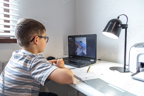 Little boy at the table with a laptop and communicates with a friend remotely.