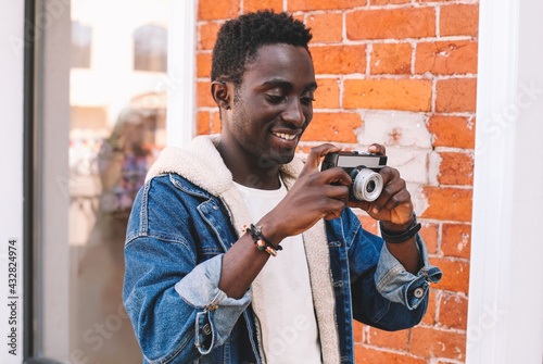 Portrait of happy smiling african man photographer with vintage film camera taking picture walking on city street