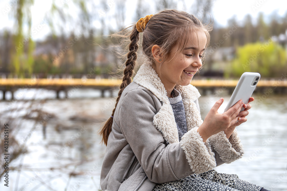 A little girl looks into the phone on a walk in the park. A little girl looks into the phone on a walk in the park.