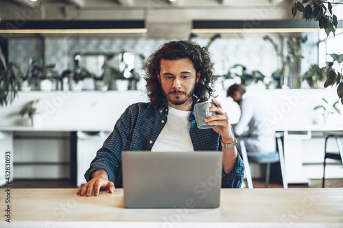 Young businessman is using laptop and holding a cup of coffee in office