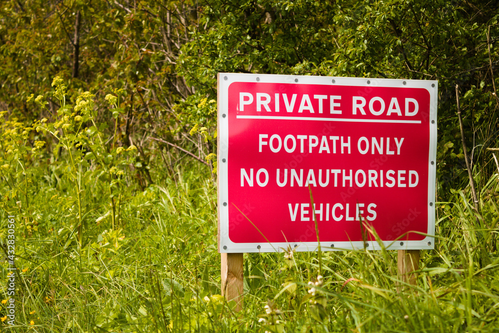 Red road sign with text: Private road, footpath only, no anauthorised vehicles isolated on foliage background