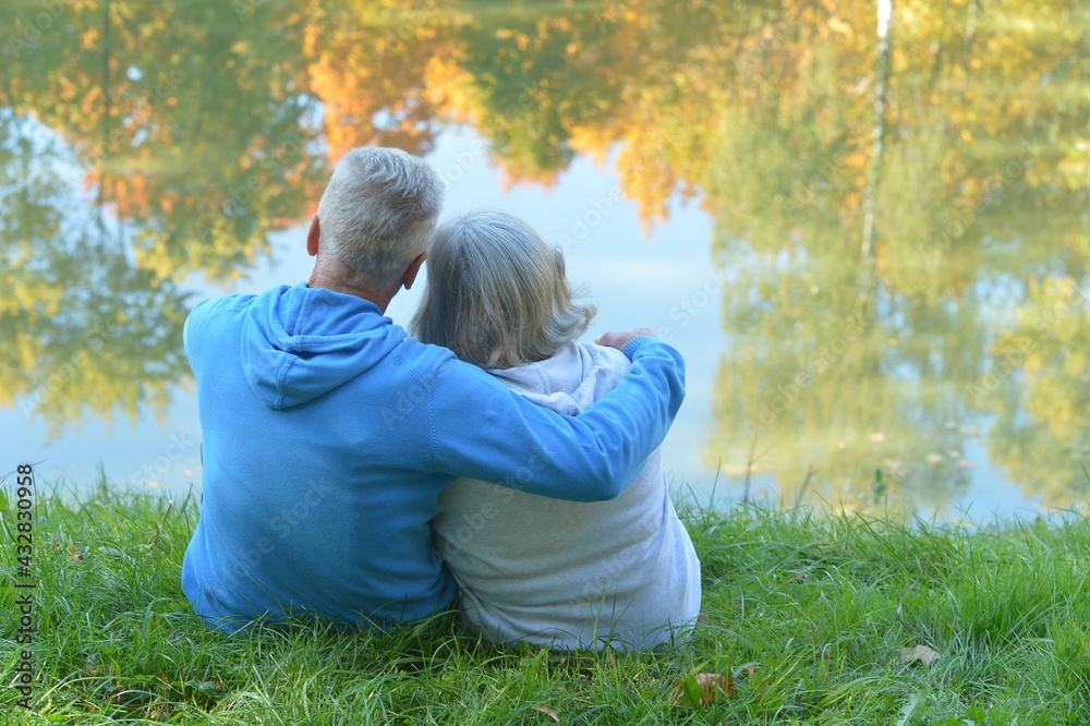 Fototapeta premium Happy senior woman and man in park sitting by pond