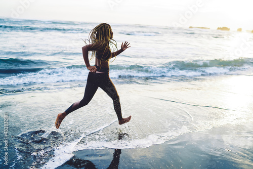 African American woman runner with casual figure doing daily morning run near ocean, young female athlete in tracksuit jogging along beach against sea keeping healthy lifestyle and body positive