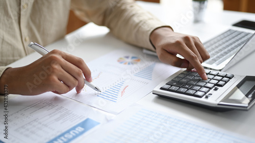 Close-up shot of Hand pointing pen to graph data and using calculator Business concepts.