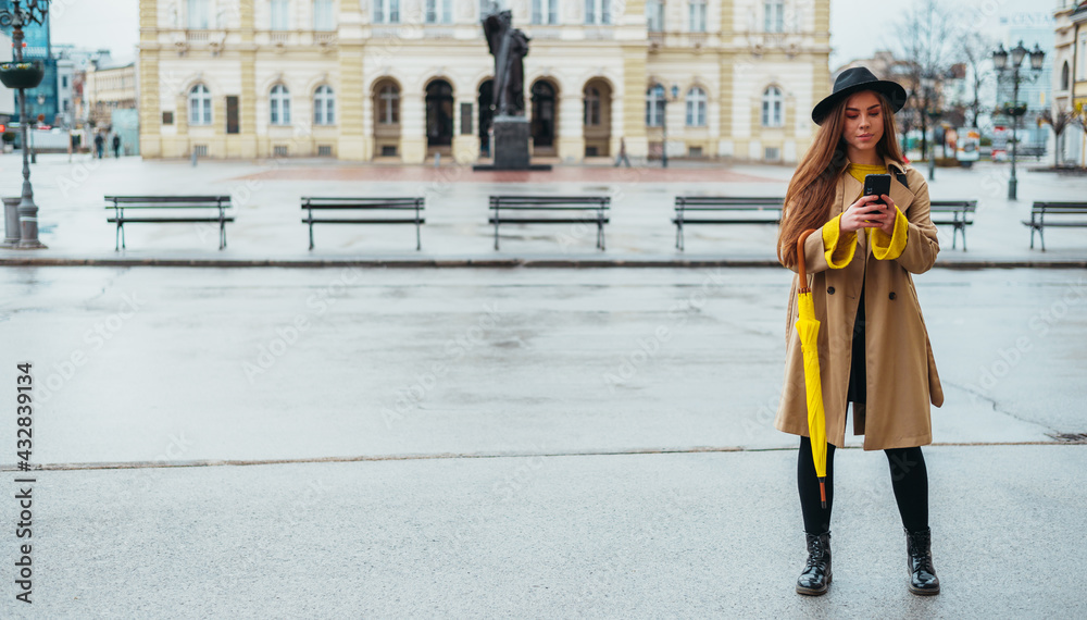 Beautiful woman using a smartphone and holding a yellow umbrella outside