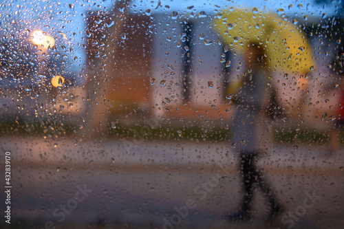 Woman holding a yellow umbrella shot through raindrops on a windo