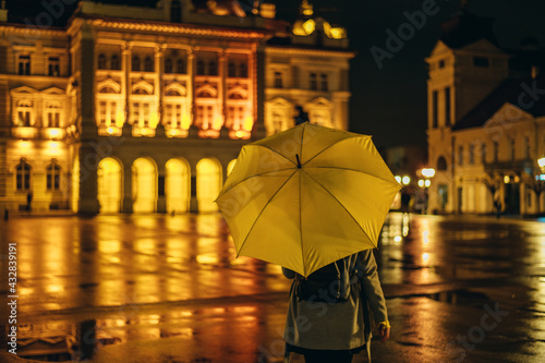 Woman holding a yellow umbrella shot from the behind in the night