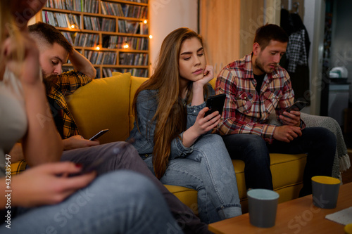 Принти на полотні Friends ignoring each other and looking at their smartphones during a party