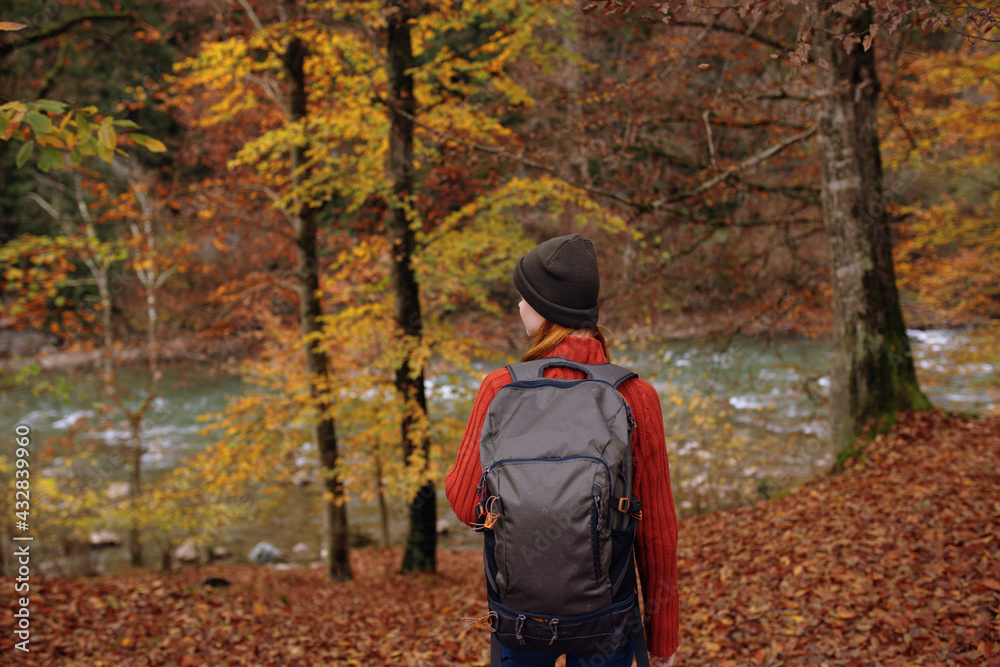woman in the park in autumn near the river and a backpack on her back back view