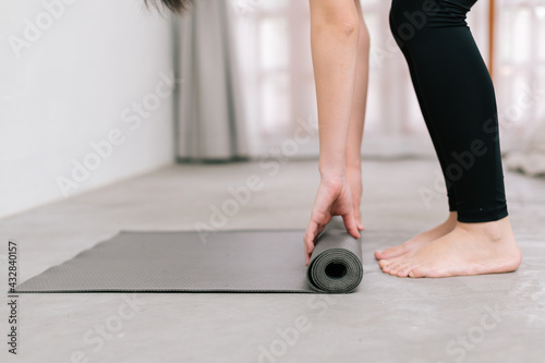 Hands of an attractive young woman folding black yoga or fitness mat after working out at home in living room or in yoga studio. Close up view photo