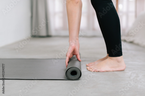 Hands of an attractive young woman folding black yoga or fitness mat after working out at home in living room or in yoga studio. Close up view photo