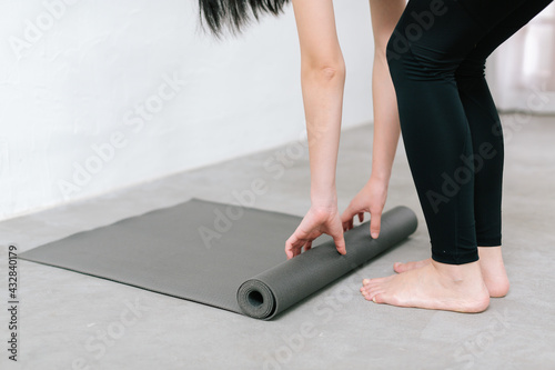 Hands of an attractive young woman folding black yoga or fitness mat after working out at home in living room or in yoga studio. Close up view photo