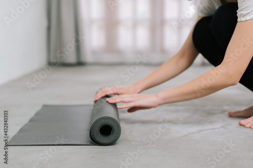 Hands of an attractive young woman folding black yoga or fitness mat after working out at home in living room or in yoga studio. Close up view photo
