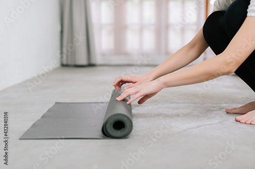 Hands of an attractive young woman folding black yoga or fitness mat after working out at home in living room or in yoga studio. Close up view photo