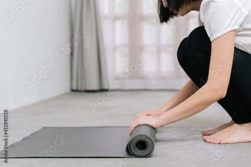 Hands of an attractive young woman folding black yoga or fitness mat after working out at home in living room or in yoga studio. Close up view photo