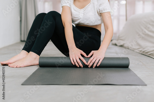 Hands of an attractive young woman folding black yoga or fitness mat after working out at home in living room or in yoga studio. Close up view photo