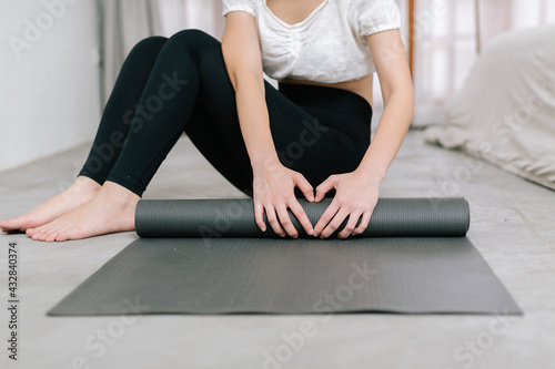 Hands of an attractive young woman folding black yoga or fitness mat after working out at home in living room or in yoga studio. Close up view photo