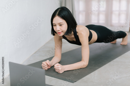 Girl training at home, exercising and watching videos on laptop, training in living room