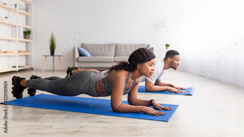 Active black couple standing in elbow plank on yoga mats at home, panorama with free space. Domestic fitness