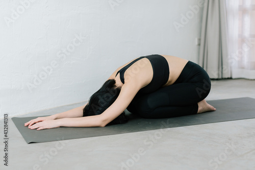 Young healthy beautiful asian woman in sportive top and leggings practicing yoga at home sitting on yoga mat relaxed, yoga concept
