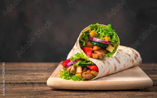 Chicken meat, French fries, vegetables and salad are wrapped in pita bread on a brown background.