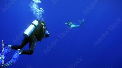 Young woman mermaid poses for camera of cameraman underwater in sea. Freediver undine water nymph with monofin on clean blue background in sea. photo