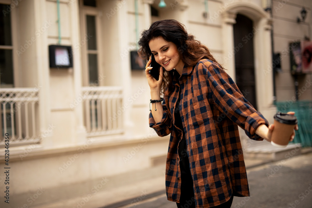 Young smiling woman enjoying outdoors. Beautiful woman talking to the phone while walking in the morning