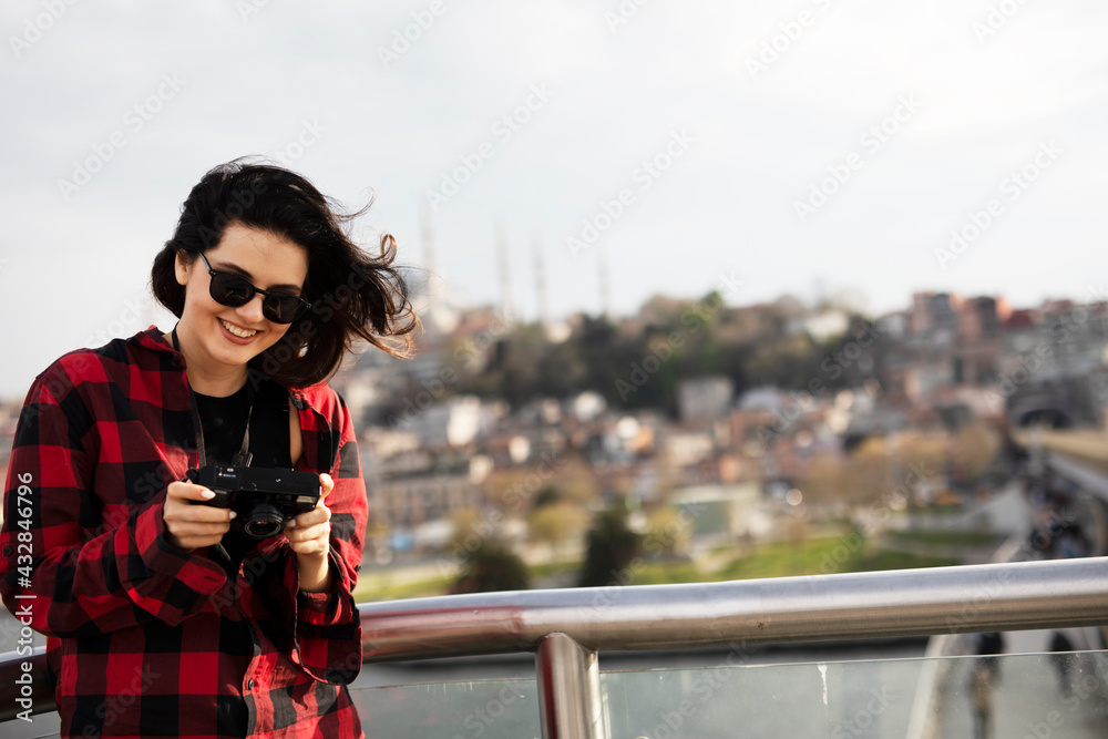 Young woman tourist standing with photo camera on the bridge. Beautiful woman traveling around the city.