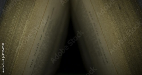 Slider shot through vintage book pages. Old book lying with their pages open in 4K against black background with 2 separate clips