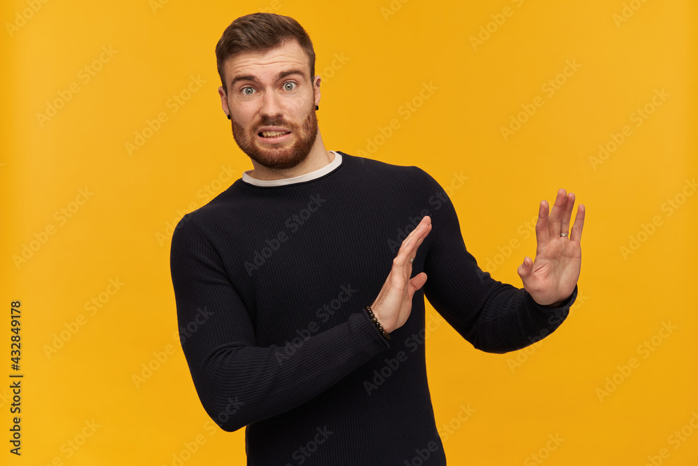 Bearded shocked guy, skeptical looking man with brunette hair. Has piercing. Wearing black sweater. Pushes arms away, reject gesture. Watching at the camera, isolated over yellow background Bearded shocked guy, skeptical looking man with brunette hair. Has piercing. Wearing black sweater. Pushes arms away, reject gesture. Watching at the camera, isolated over yellow background