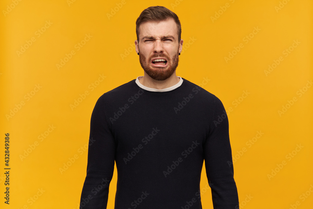Portrait of upset, crying male with brunette hair and bristle. Has piercing. Wearing black sweater. Emotion concept. Watching at the camera, isolated over yellow background Portrait of upset, crying male with brunette hair and bristle. Has piercing. Wearing black sweater. Emotion concept. Watching at the camera, isolated over yellow background