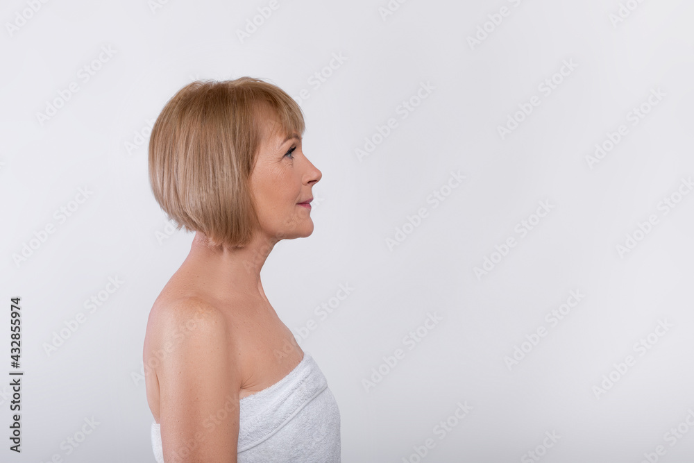 Side view of charming mature lady in bath towel on light studio background, copy space Side view of charming mature lady in bath towel on light studio background, copy space